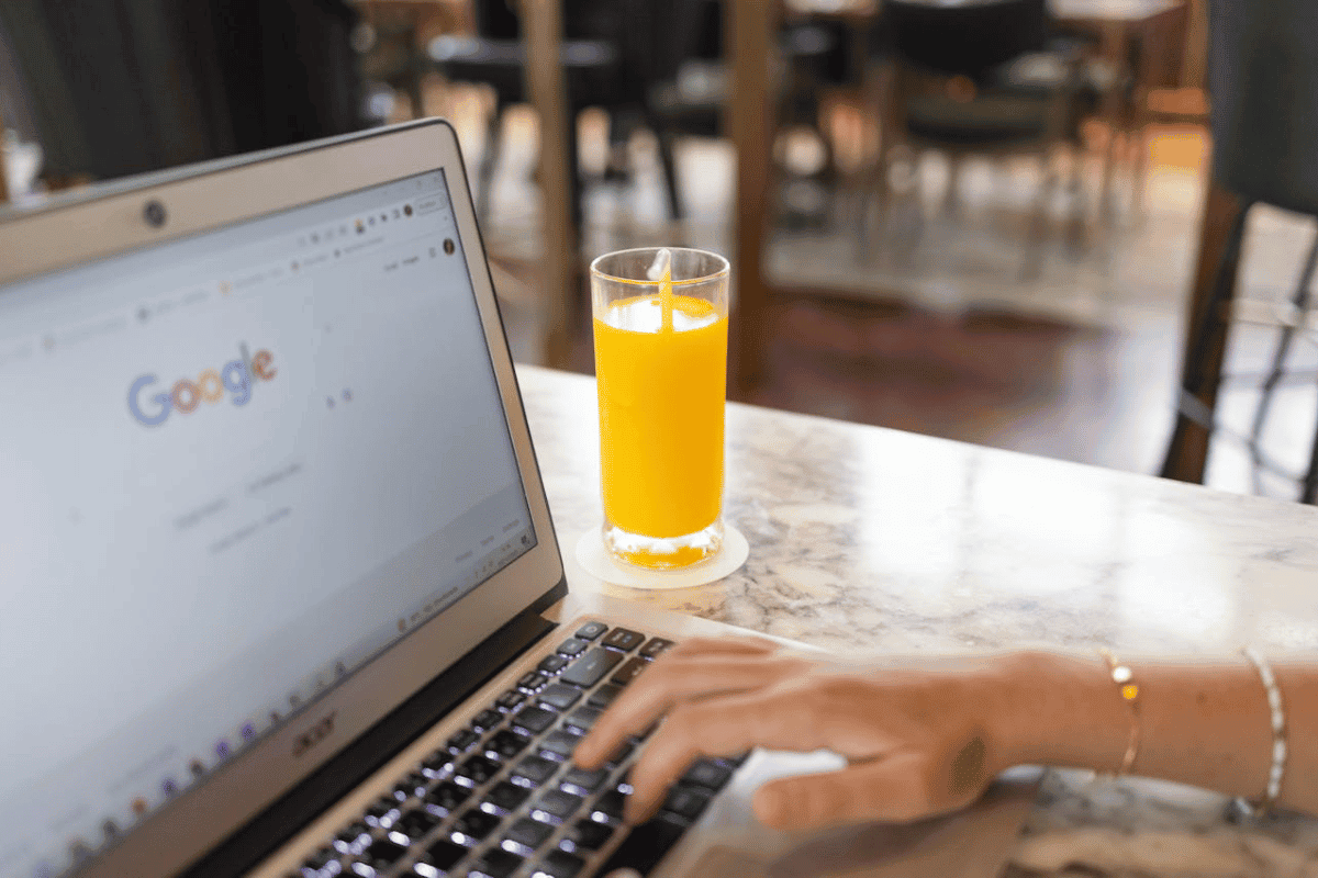 A woman googling on a laptop next to a glass of juice